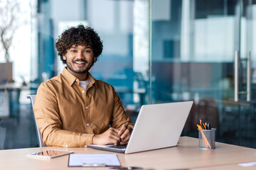 Portrait of young successful businessman inside office at workplace, hispanic smiling and looking at camera, male programmer happy with achievement results.