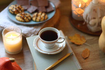 Cup of tea or coffee, plate with desserts, dried oranges, bowl of grapes, scented candles, vintage books, pumpkins and autumn leaves on the table. Autumnal hygge. Selective focus.