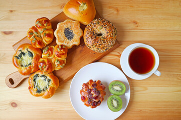 Top view of assorted buns with a cup of hot tea on wooden table