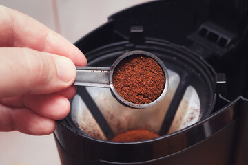 The process of filter coffee preparation. Portion of ground coffee spilled in electrical dripper. Closeup view with selective focus on spoon. - 679290959