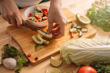 Lady slicing an avocado on a wooden table with fresh vegetables on it.