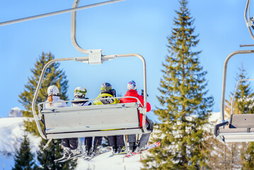 Skiers going up the mountain on a chairlift on a sunny winter day