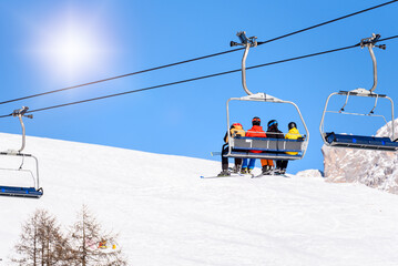 Skiers in colourful ski suits riding a chairlift in a ski resort on a sunny winter day
