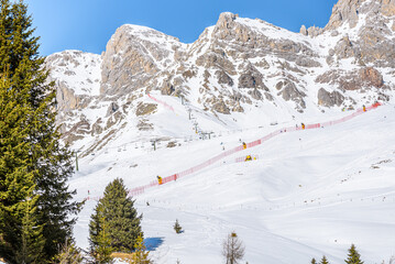 Chairlifts and ski runs at the foot of  towering snowy peaks in the Alps on a sunny winter day