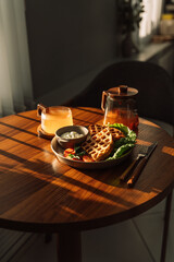 Breakfast with waffles and tea at a wooden table under the sunlight.
