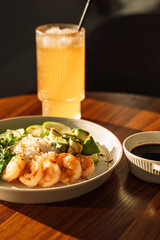 Light snack of avocado and shrimp with cool drink in round plate on wooden table.