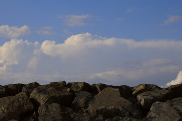 Fototapeta na wymiar cobble rock, stone way on a background blue cloudy sky. Narrow road under the blue heaven. horizon line.