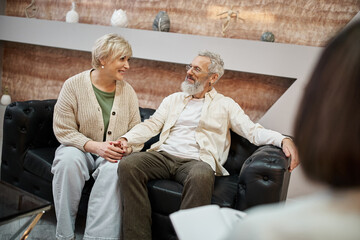 happy middle aged couple sitting on couch together near family counselor, relationship support