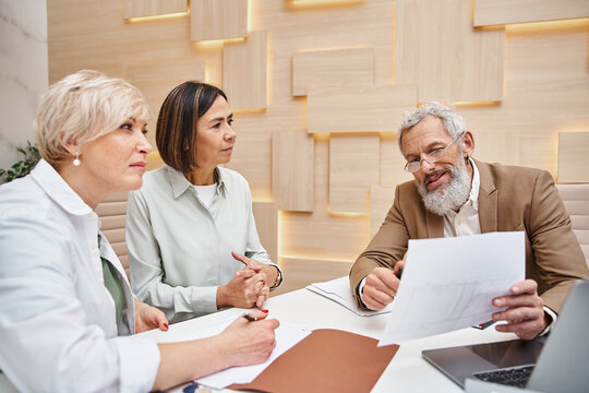 bearded realtor holding contract near lesbian couple in real estate office, middle aged lgbt family