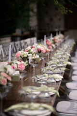 A large, long, decorated, wooden table and chairs, covered with a white tablecloth with dishes, flowers, candles.