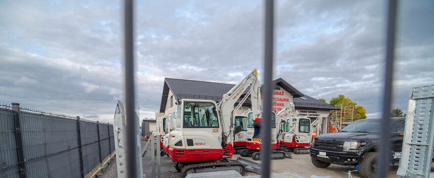 Polska Ostrowiec Świętokrzyski 4 października 2023 godz 14:46. Małe koparki firmy Takeuchi na gąsienicach gumowych  stoją na placu przed wypożyczalnią budowlanego sprzętu, za ogrodzeniem na tle chmur.