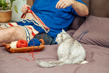 Young man knitting a striped sweater at home.