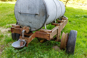 Old rusty mobile water tank with its cattle waterer on an agricultural plot on a Dutch farm, trees...