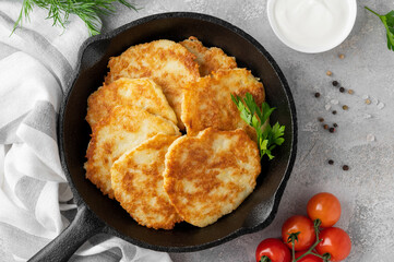 Potato pancakes, latkes or draniki with fresh herbs and sour cream in a cast iron pan on a gray concrete background. Top view, copy space.