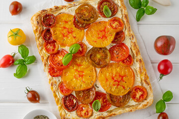 Tomatoes pie or galette from puff pastry and cheese filling on a white wooden background. Vegetarian healthy food. Selective focus.