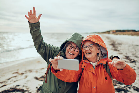 Senior friends holding smartphone on winter beach walk