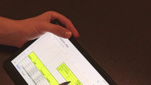 Business person working on wooden table Indoors, using tablet and stylos, looking on the screen showing bank loan amortization table. Finance