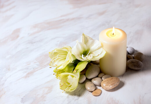 Vanilla candle burning with tropical flovers and pebbles stones