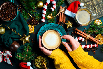 Christmas concept. Cup of fragrant cappuccino coffee in female hands. New Year's decor. On a dark...