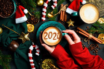 Woman holding cup of cappuccino with cinnamon. Numbers 2024. New Year's decor. On a dark background.