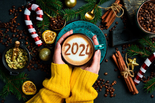 Numbers 2024. Woman holding Cup of cappuccino with cinnamon. New Year's decor. On a dark background.