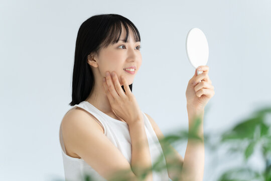鏡で肌をチェックする白い服の若い女性