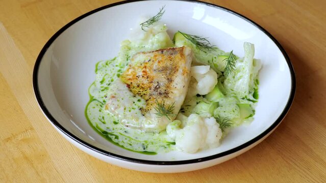 The cook prepares a dish with fish. Close-up professional chef in a restaurant kitchen serving a dish adding the last ingredient by hand. The male chef makes the composition of the dish for serving.