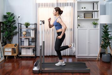 Full length side view of energetic and strong athletic asian woman running running machine at home. Pursuit of fit physique and commitment to healthy lifestyle with home workout and training. Vigorous