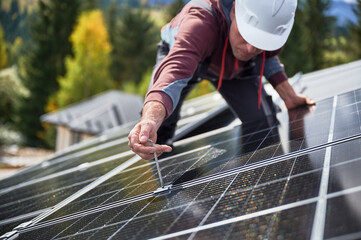 Man electrician mounting photovoltaic solar panels on roof of house. Engineer in helmet installing...