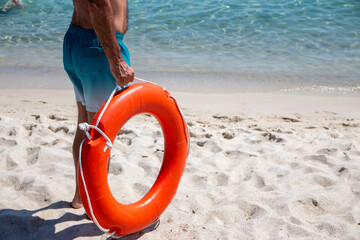 lifeguard holding orange lifebuoy on the beach