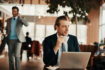 Middle aged businessman sitting in cafe holding mug looking away