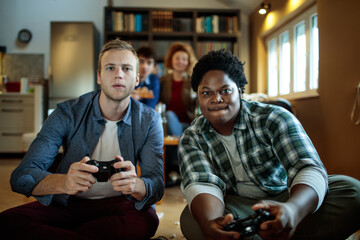 Friends playing video games on console using controller while sitting at home
