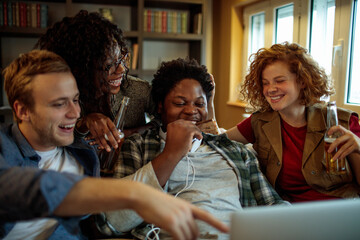 Young and diverse group of friends watching a movie on laptop in the living room on the couch - obrazy, fototapety, plakaty