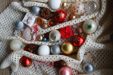Various colorful Christmas ornaments, small presents and seasonal spices on white knitted blanket. Top view.