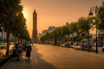 The Avenue Habib Bourguiba Clocktower in Tunis downtown, the famous landmark of Tunisia, with the people walking by on the promenade during the colorful sunset.