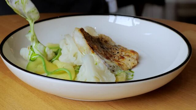 The cook prepares a dish with fish. Close-up professional chef in a restaurant kitchen serving a dish adding the last ingredient by hand. The male chef makes the composition of the dish for serving.