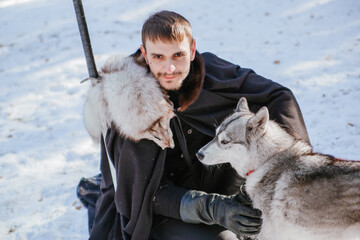 A man in a black cloak with a sword and skin. Warrior in the forest with a wolf in winter.