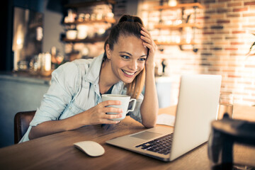 Happy Woman Enjoying Coffee While Working on Laptop at Home