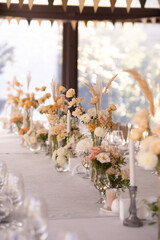 A large, long, decorated, wooden table and chairs, covered with a white tablecloth with dishes, flowers, candles.
