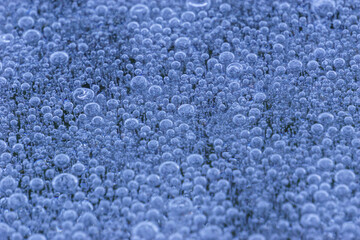 Abstract background of bubbles of air under layer ice in clear water lake