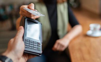Young woman holding credit doing wireless bank payment with POS terminal process acquire at table in coffee shop cafe restaurant indoor. Focus on machine. Finance, restaurant industry, small business.