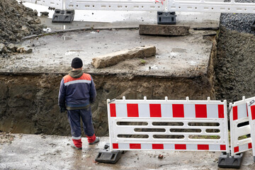 A worker stands near a trench where communications are laid under the road surface.
