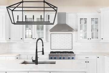 A kitchen detail with a black faucet and light fixture on the island, white cabinets, and a mosaic...