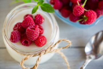 Sweet cooked homemade yogurt with fresh raspberries in a glass jar.