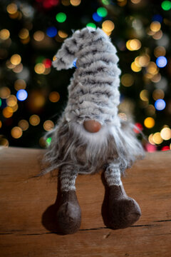 Petit P&egrave;re-No&euml;l gris et blanc, avec un bonnet gris et blanc tr&egrave;s grand qui cache ses yeux, petit nez avec une barbe blanche, assis sur un tronc d'arbre devant des d&eacute;corations lumineuses  de No&euml;l 