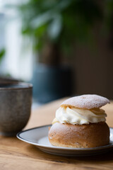 Traditional Swedish pastry, known as semla, on a plate at wooden table. In the background is a coffee mug. Photo taken in Sweden.