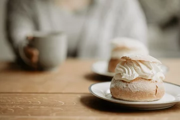 Foto op Plexiglas Traditional Swedish pastry, known as semla, on a plate at wooden table. In the background, out of focus, is a person with grey sweater, holding a coffee cup. Photo taken in Sweden. © Susie Hedberg