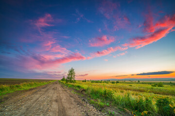 Rural landscape with ground road in a countryside at summer sunset