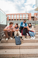 Vertical. Group of multiracial high school students talking on a staircase at university campus,...