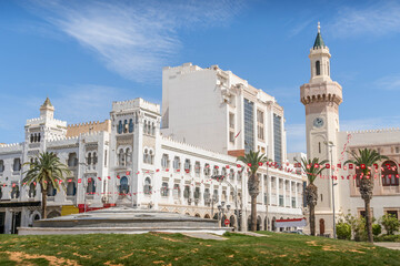 The white-painted colonial architecture buildings in the downtown of Sfax, Tunisia, with the Tunisian flags, beautiful balconies, and the small park. - obrazy, fototapety, plakaty